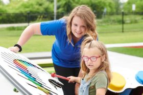 Preschool teacher and child engaged in an outdoor musical learning activity as part of New Horizon Academy's summer program